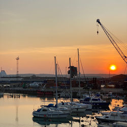 Sailboats moored at harbor against sky during sunset