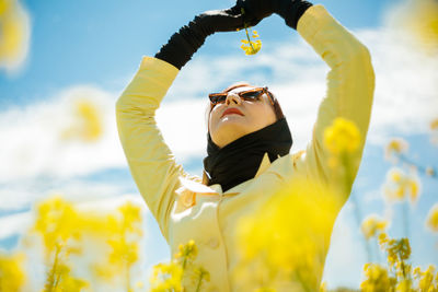 Low angle view portrait of a stylish woman among a blooming yellow field under a bright spring sky