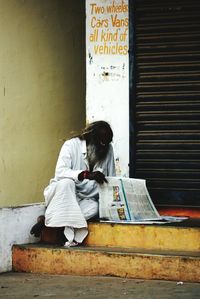 Man reading newspaper while sitting on steps against closed shutter