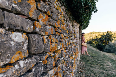 Selective focus of young woman in pinke dress leaning on stone wall, selective focus.