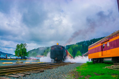 Trains on railroad track against cloudy sky