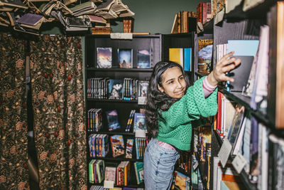 Girl reaching for books arranged on shelf in bookstore