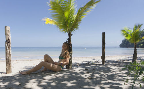 Woman in bikini sitting on sand at beach