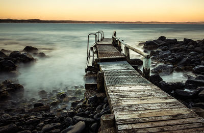 Jetty on sea against sky at sunset