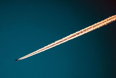 Low angle view of airplane with vapor trail in clear blue sky