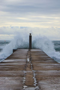 View of waves splashing on pier against sky