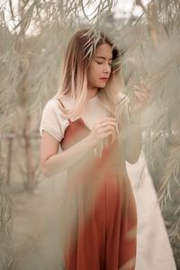 Side view of young woman with arms raised standing against trees