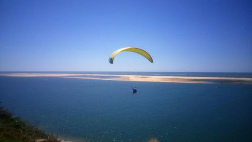 Person paragliding over sea against clear blue sky