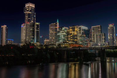 Illuminated buildings by river against sky in city at night