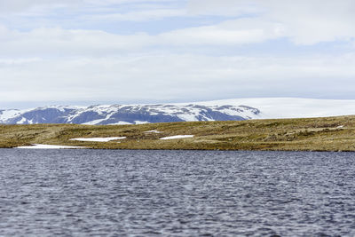 Scenic view of sea by snowcapped mountain against sky