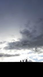 Silhouette people riding on field against sky