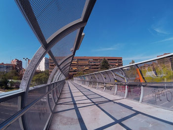 Futuristic bridge in madrid, spain, with a curved structure and a building at the back. blue sky