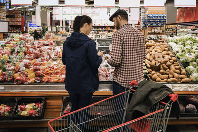 Rear view of couple choosing vegetables while standing at supermarket