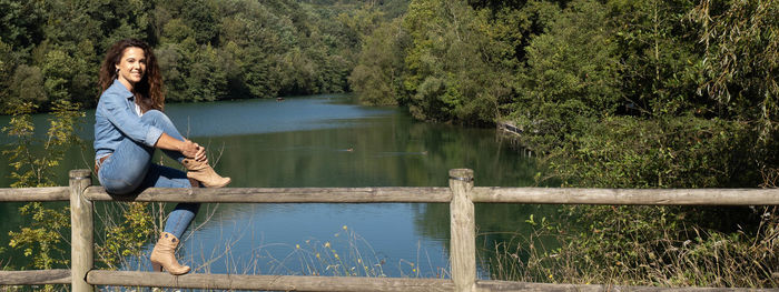 Woman sitting by lake against trees