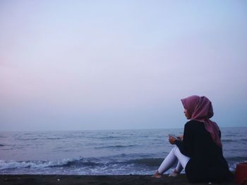 Rear view of woman sitting on beach against clear sky