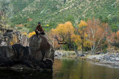 Woman sitting on rock in lake at forest against mountain