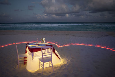 Table and chairs at beach against sky at night