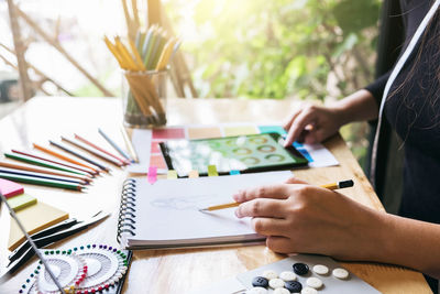 Midsection of fashion designer sketching in book at studio