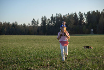 Happy mother carrying son on shoulders while walking on grassy field in park