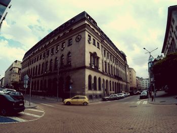 Cars on city street by buildings against sky