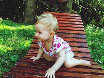 Baby girl sitting on wooden deck chair at field