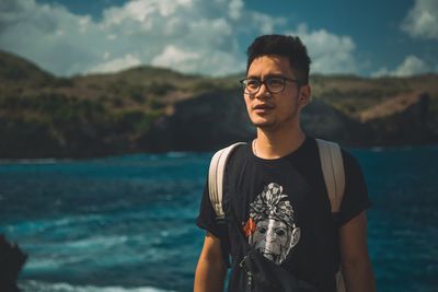 Young man looking away while standing against sea and sky