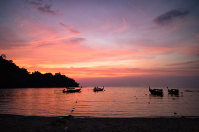 Silhouette boats moored on sea against orange sky