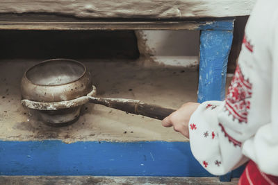 Hostess in embroidered clothes pulled a pot of food out of the oven. retro photo of ukrainian life