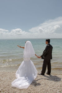Rear view of couple standing at beach against sky