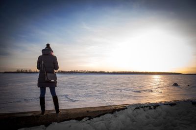 Rear view of man standing at beach during sunset