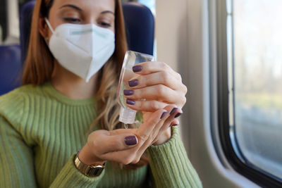 Business woman with medical face mask using alcohol gel sanitizer hands on public transport. 