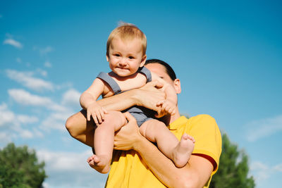 Delighted father standing in park and playing with little kid while enjoying weekend together in summer