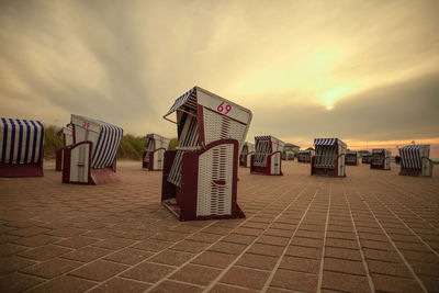 Hooded chairs on beach against sky at sunset