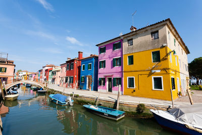 Boats moored in canal by houses against sky in city