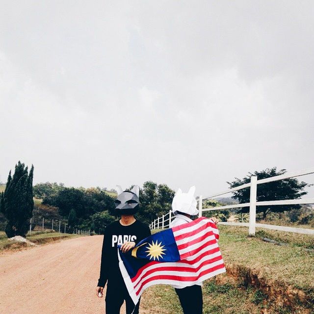 lifestyles, sky, leisure activity, standing, field, red, road, casual clothing, rear view, day, grass, men, flag, patriotism, tree, outdoors, national flag, landscape