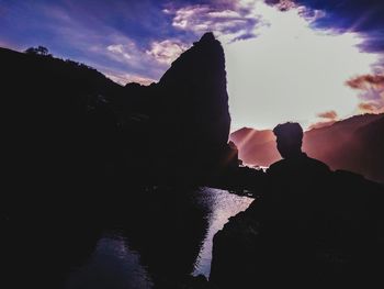 Silhouette people standing on rock against sky during sunset