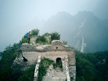 Side view of man standing on old ruin against mountain during foggy weather