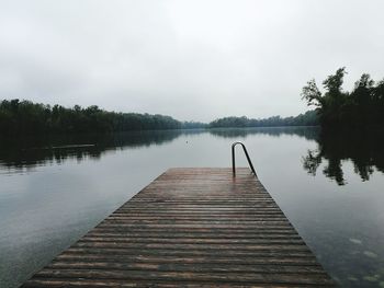 Pier on calm lake against clear sky