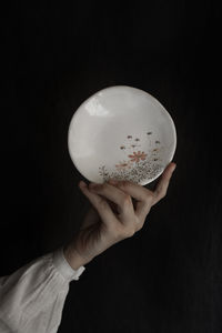 Close-up of hand holding plate against black background