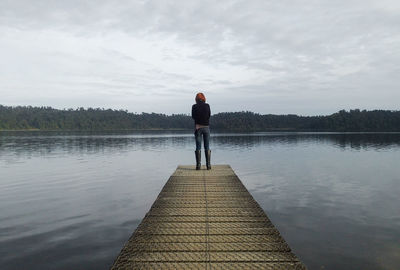 Rear view of woman standing on pier by lake against sky