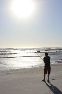 Rear view of woman walking on beach against sky during sunset