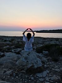 Woman making heart shape at beach against sky