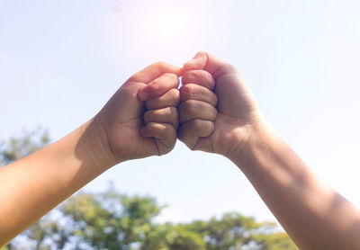 Close-up of hands fist bumping against sky