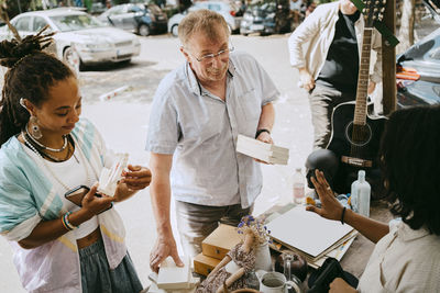 High angle view of customer holding books while bargaining with owner at flea market