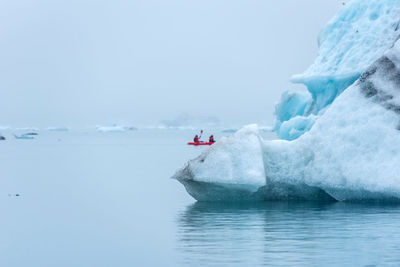 People kayaking in sea by iceberg