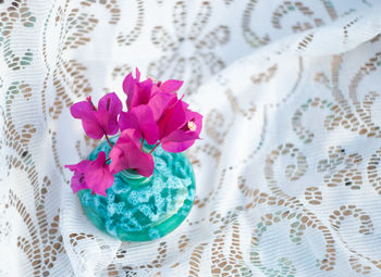 Purple bougainvillea flowers in turquoise vase against the background of a lace