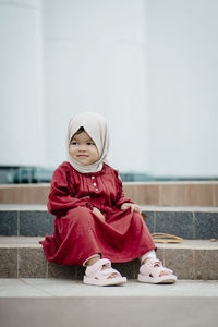 Portrait of young woman sitting against wall