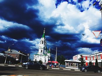 Cars on road by buildings against sky in city