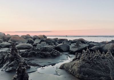 Rocks on sea shore against sky during sunset