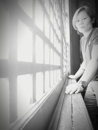 Side view of young woman looking through window at home